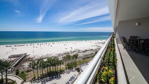 A balcony with a view of a beach, lounge chairs, and a railing.