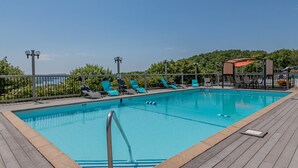 A rectangular swimming pool with a wooden deck, surrounded by lounge chairs and a metal fence. - Modern Luxury Condo with Private Deck, Amazing Views, Near SDC with Free Tickets (Branson)