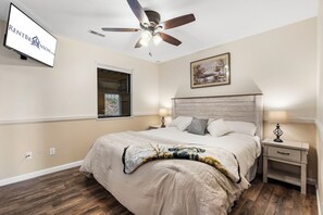A bedroom with a bed, two bedside tables, a ceiling fan, a window, and a painting on the wall.