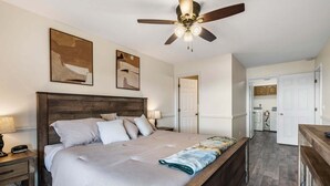 Ein Schlafzimmer mit einem großen Bett, einem Nachttisch, einem Schreibtisch, einem Deckenventilator und einer Tür zu einem Badezimmer.