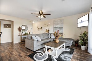 A modern living room with a grey sectional sofa, a wooden coffee table, and a ceiling fan. - Modern Luxury Condo with Private Deck, Amazing Views, Near SDC with Free Tickets (Branson)