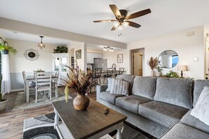 Un salon moderne avec un canapé gris, une table basse en bois et un coin repas comprenant une table et des chaises blanches.
