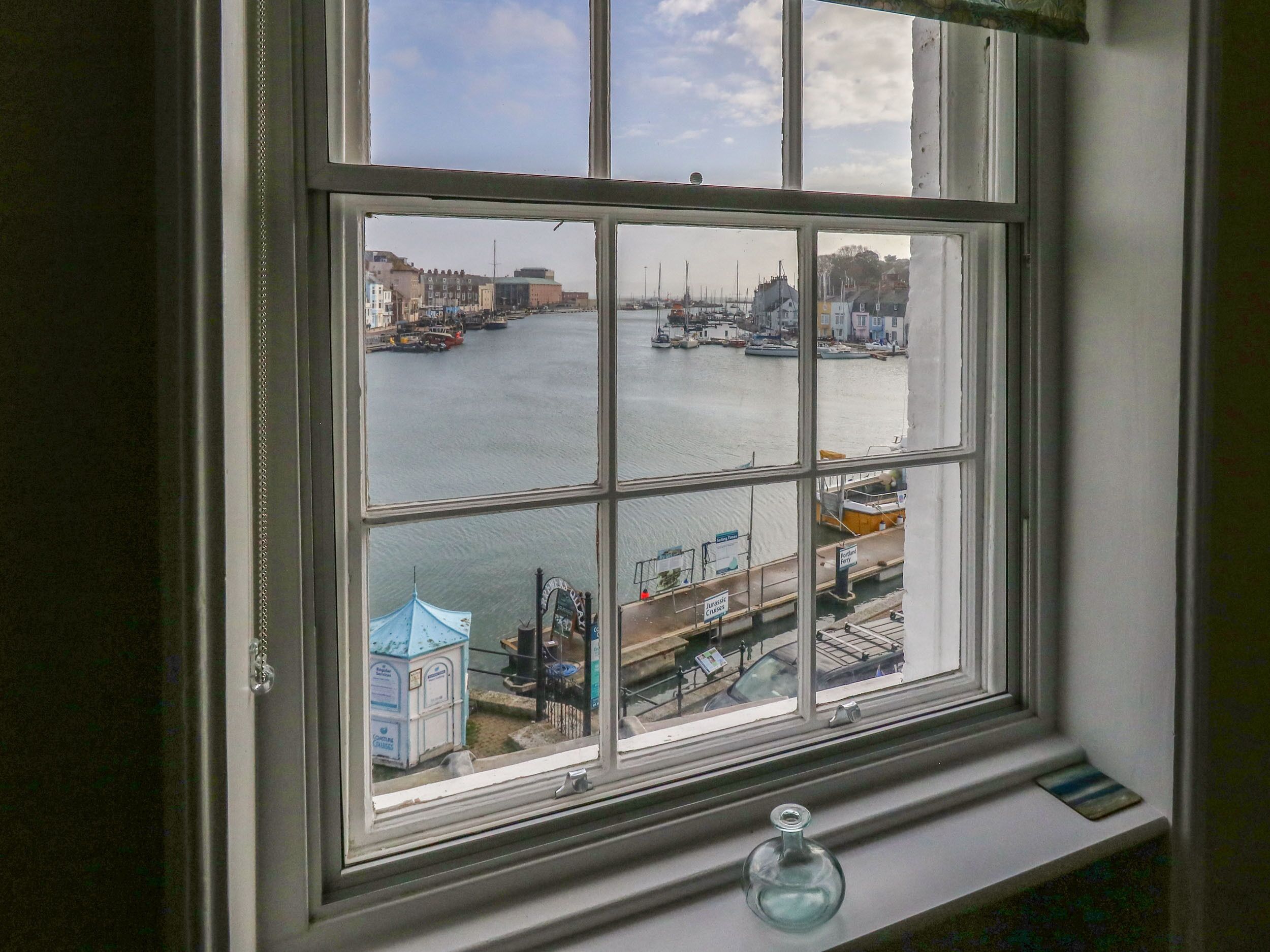 A window with a view of a harbor, including boats and buildings.