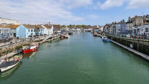 A harbor with boats docked along the waterfront, buildings lining the shore, and a clear sky. - Embassy (Weymouth)