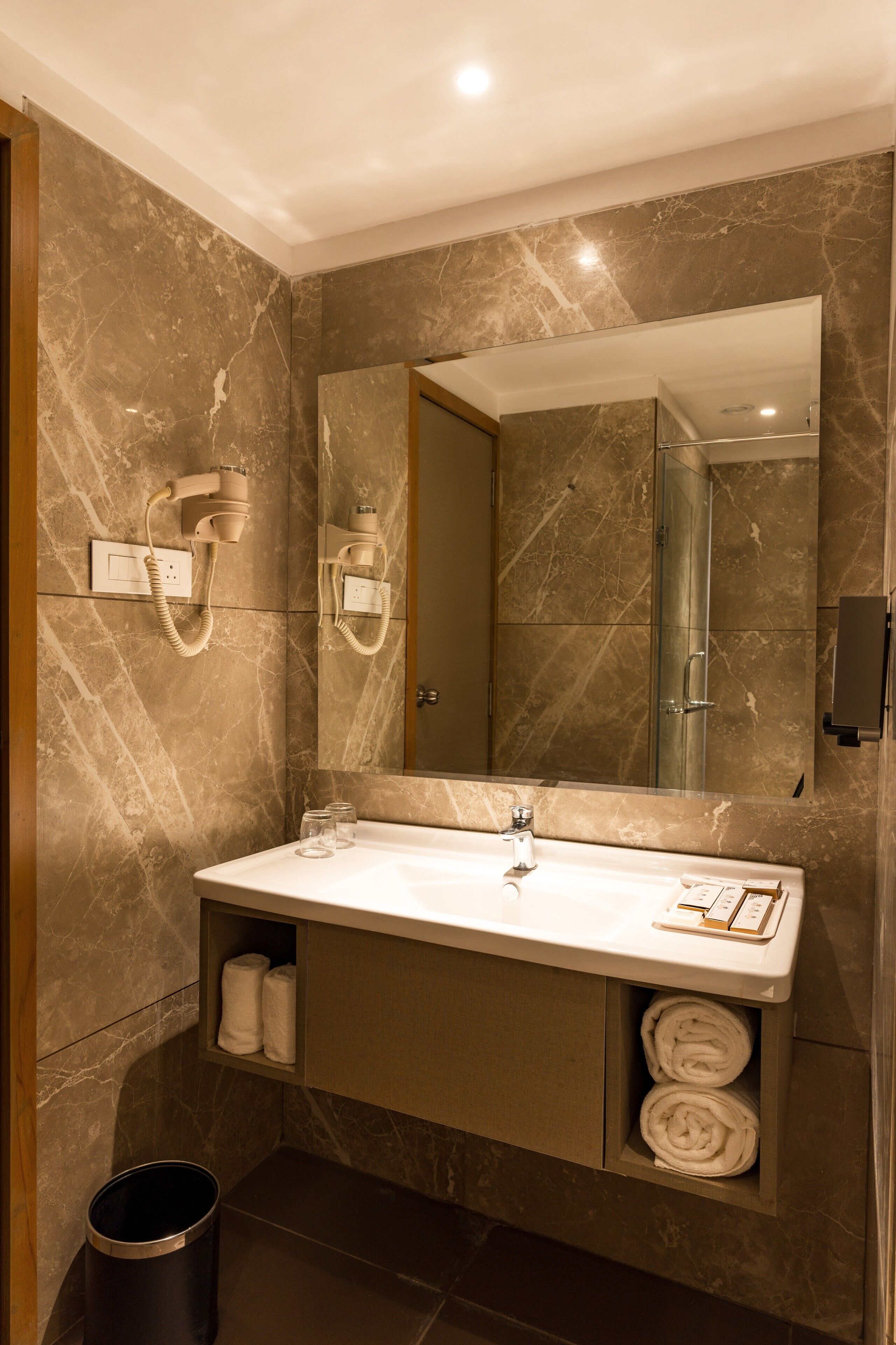 Un bany modern amb una paret de marbre, un mirall gran, un lavabo amb porta tovalloles i una zona de dutxa.