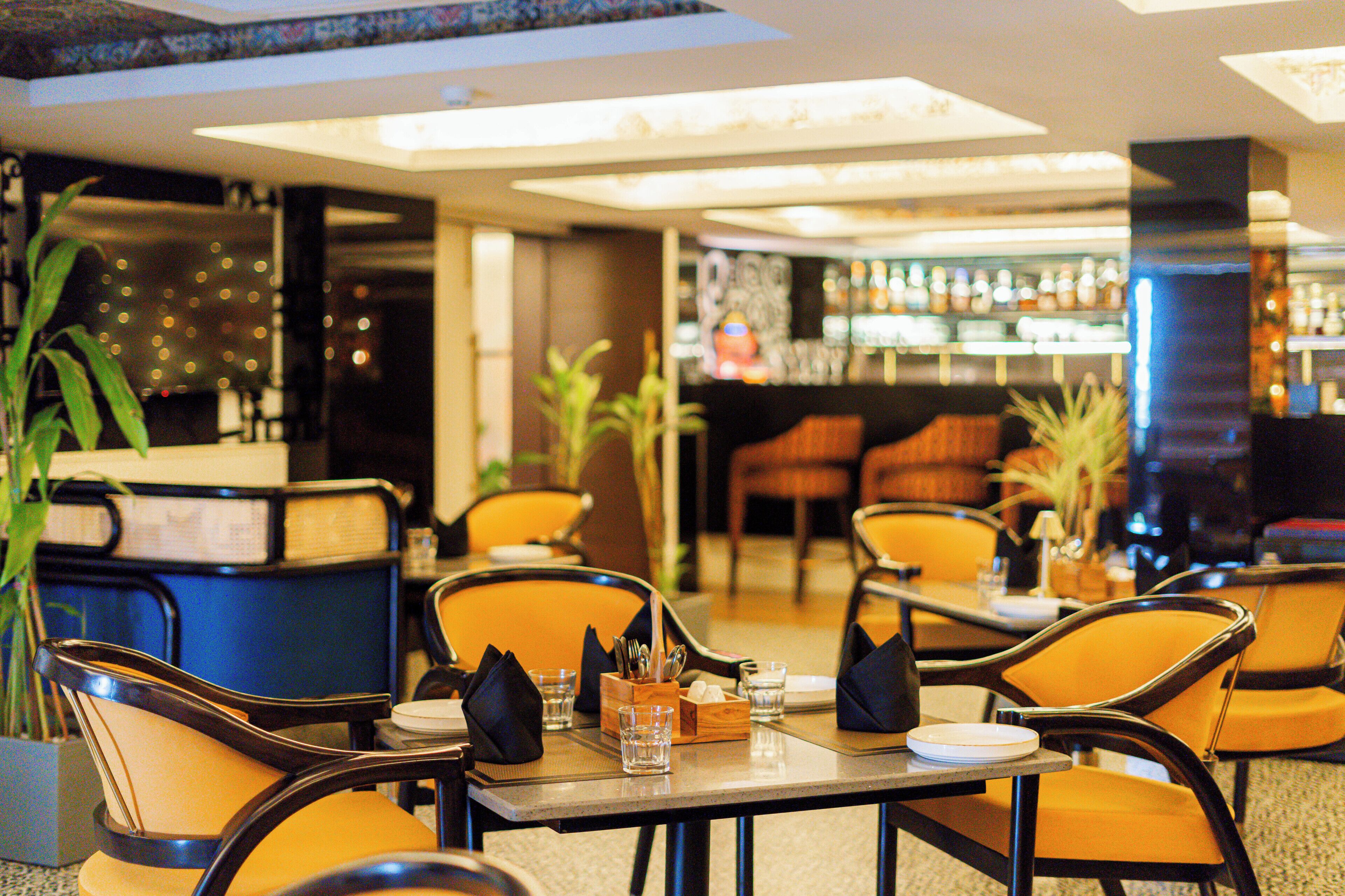 A restaurant with tables and chairs, a bar area, and potted plants.