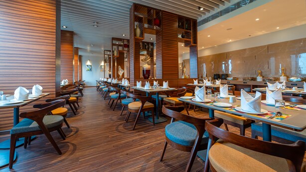A modern restaurant with wooden flooring, neatly arranged tables and chairs, and a variety of decorative items on shelves. - Effotel By Sayaji Bhopal (Bhopal)