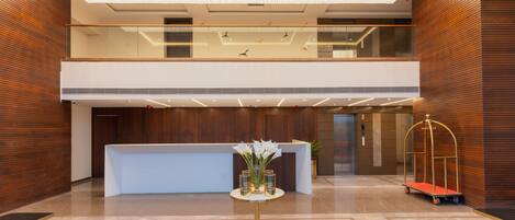 A modern lobby with a reception desk, a decorative ceiling light, and a cart.