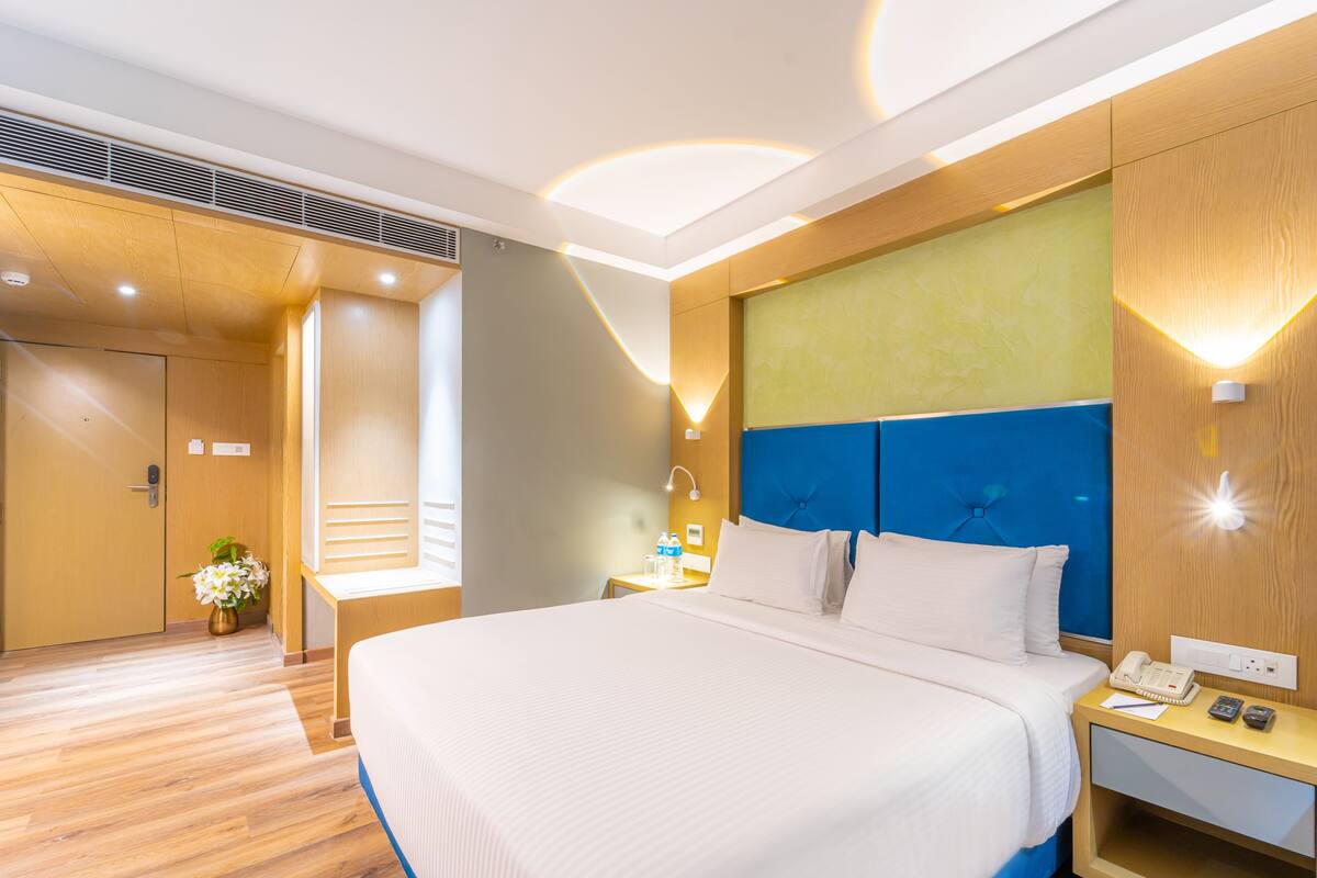 Una moderna camera d'albergo con un letto grande, pavimento in legno, parete azzurra e comodino con telefono e lampada.