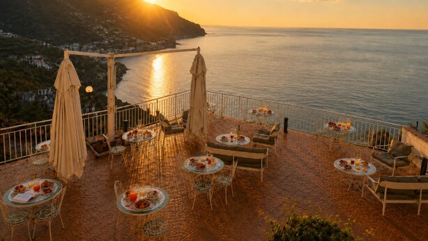 A terrace with outdoor seating, tables with food, and a view of the sea and mountains at sunset. - Gala Residence Villa Giovanna (Ravello)