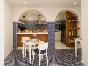 A modern kitchen with a dining area, featuring a patterned backsplash, a central island with fruit, and a wine rack.