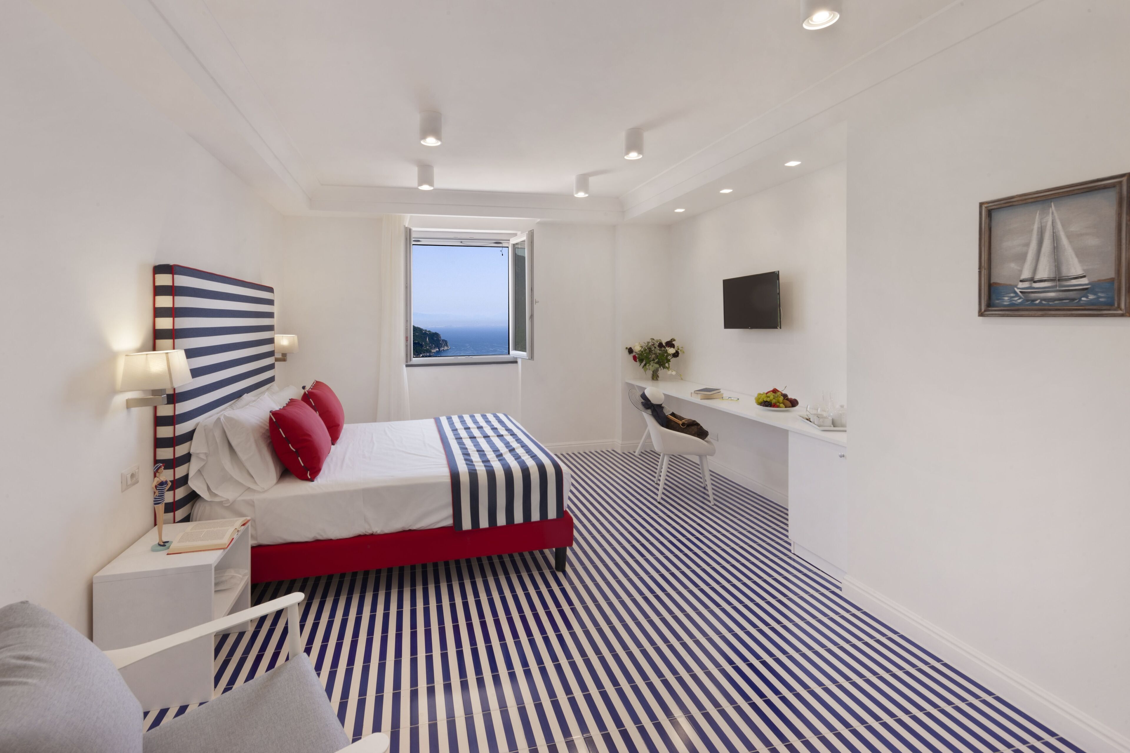 Een moderne slaapkamer met een bed, een bureau, een stoel, een raam met uitzicht en een aan de muur bevestigde televisie.