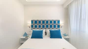 A modern hotel room with a large bed, two blue pillows, a patterned headboard, and a white nightstand with a lamp.