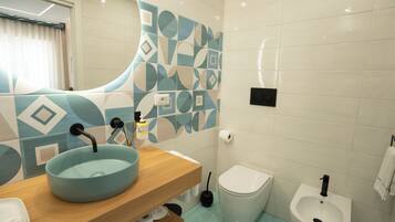 A bathroom with a sink, toilet, bidet, and a mirror with a geometric tile backsplash.