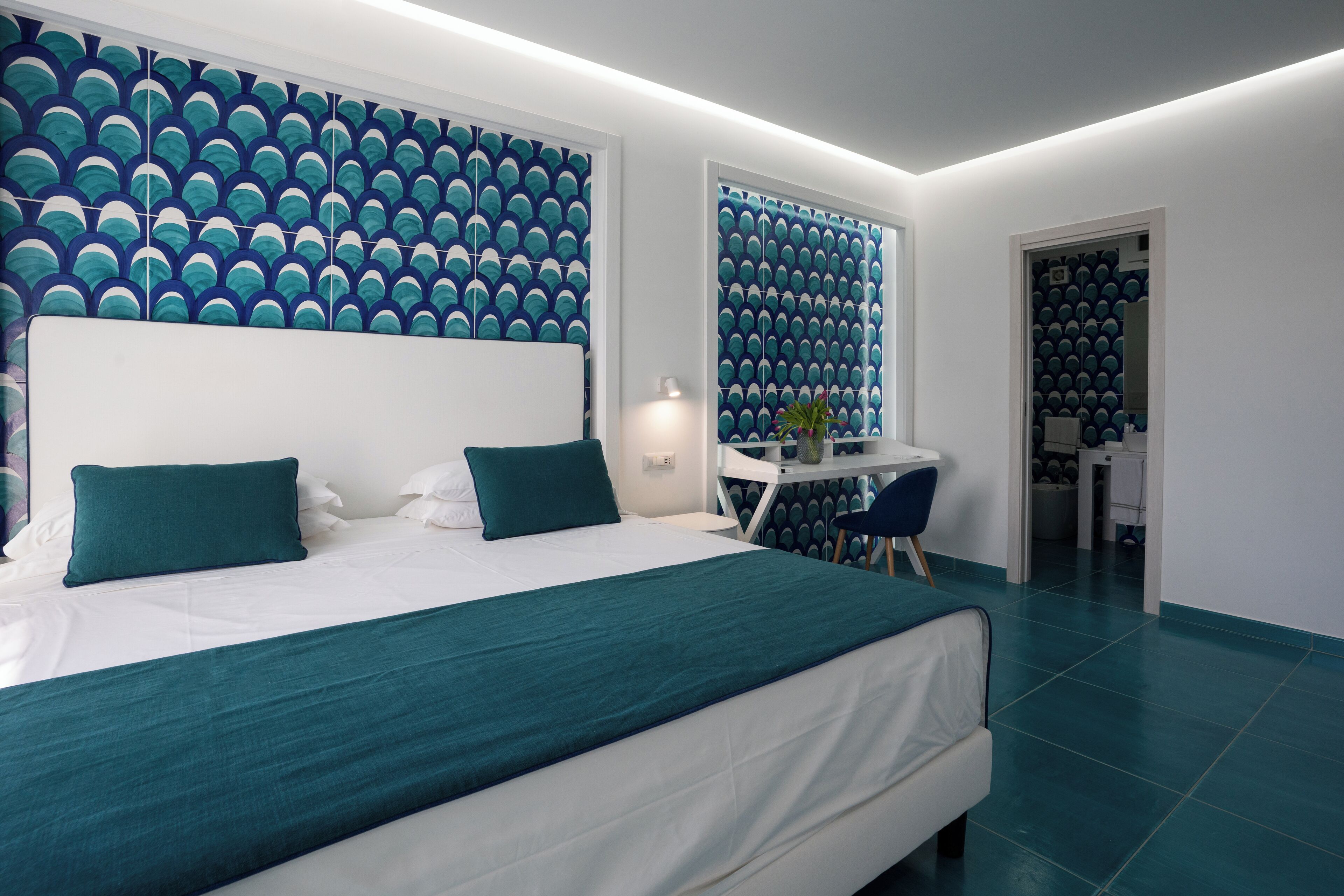 A modern hotel room with a large bed, a desk, and a chair.