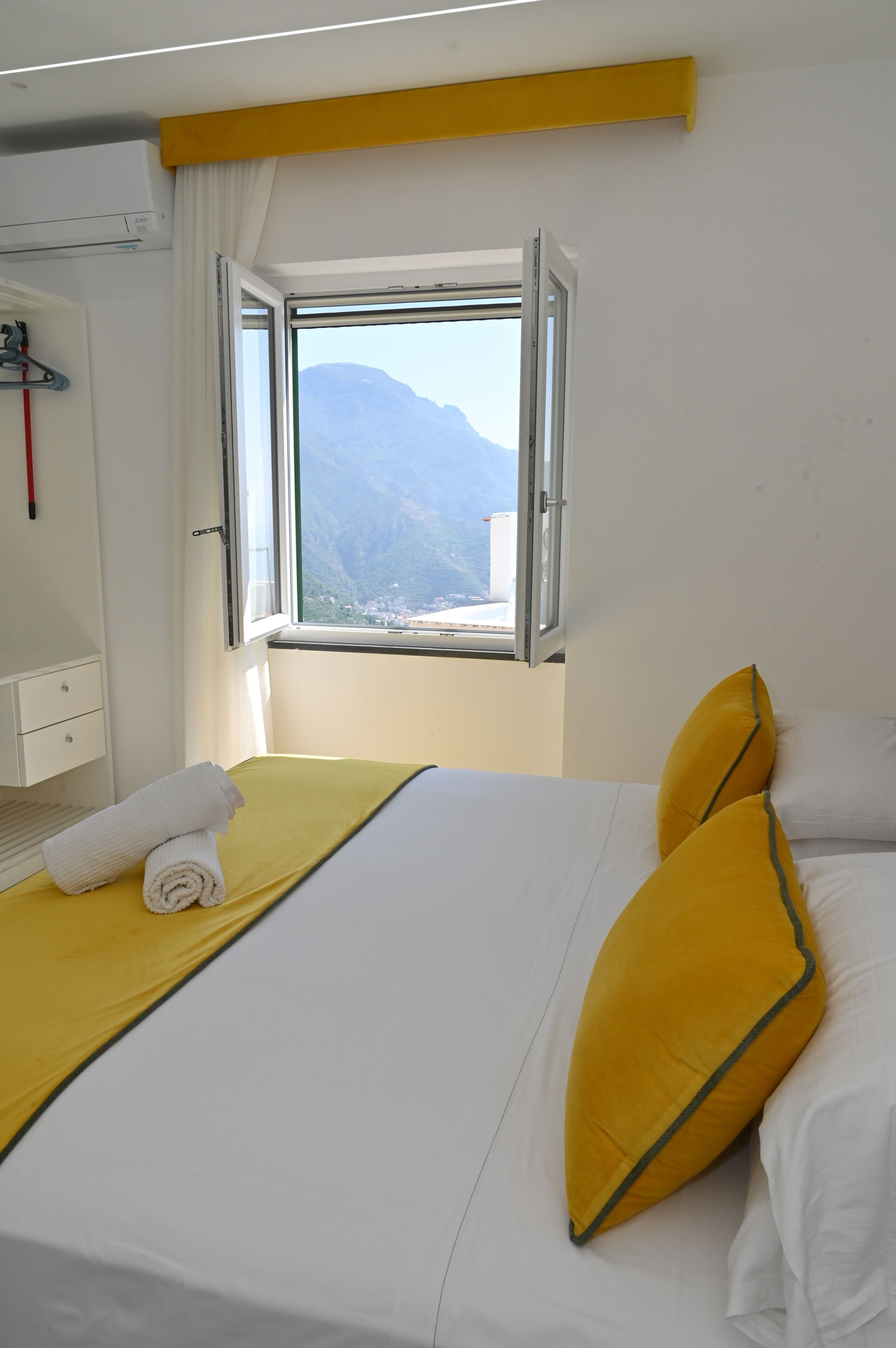A hotel room with a bed, a window with a mountain view, a towel on the bed, and a white wall.