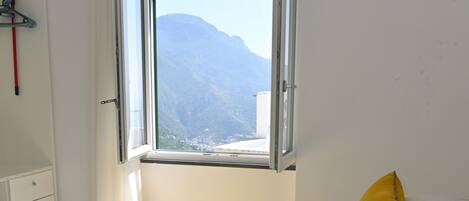 A hotel room with a bed, a window with a mountain view, a towel on the bed, and a white wall.