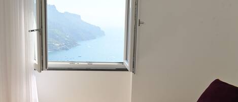 Habitación de hotel con una cama, una ventana que ofrece vistas al mar y acantilados, y una colcha morada.