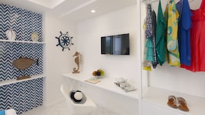 A modern room with a white wall, a mounted TV, a white chair, and a shelf with decorative items. - Gala Residence Villa Giovanna (Ravello)
