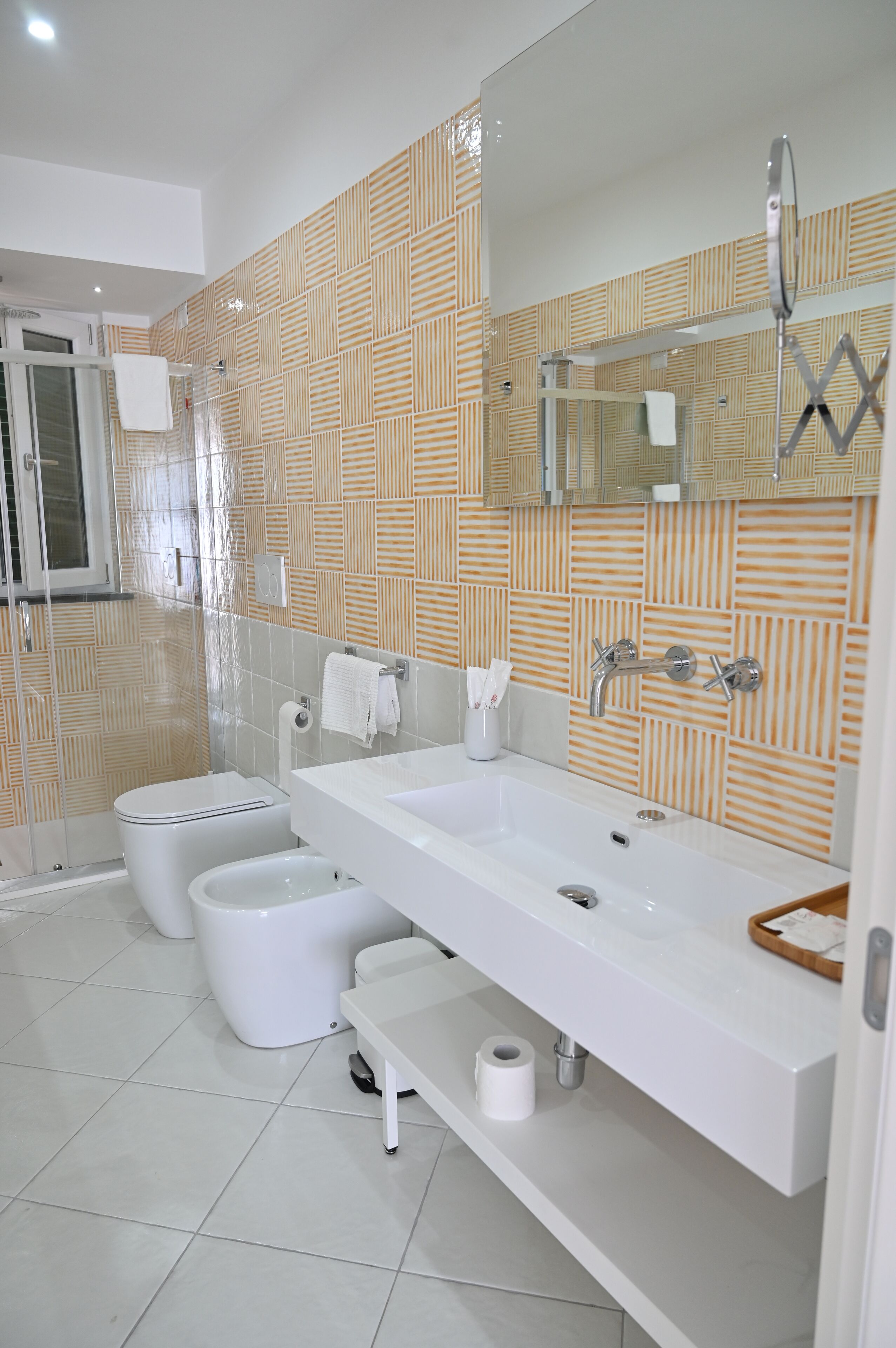 Une salle de bain moderne avec un grand lavabo, deux toilettes, une douche et un miroir.
