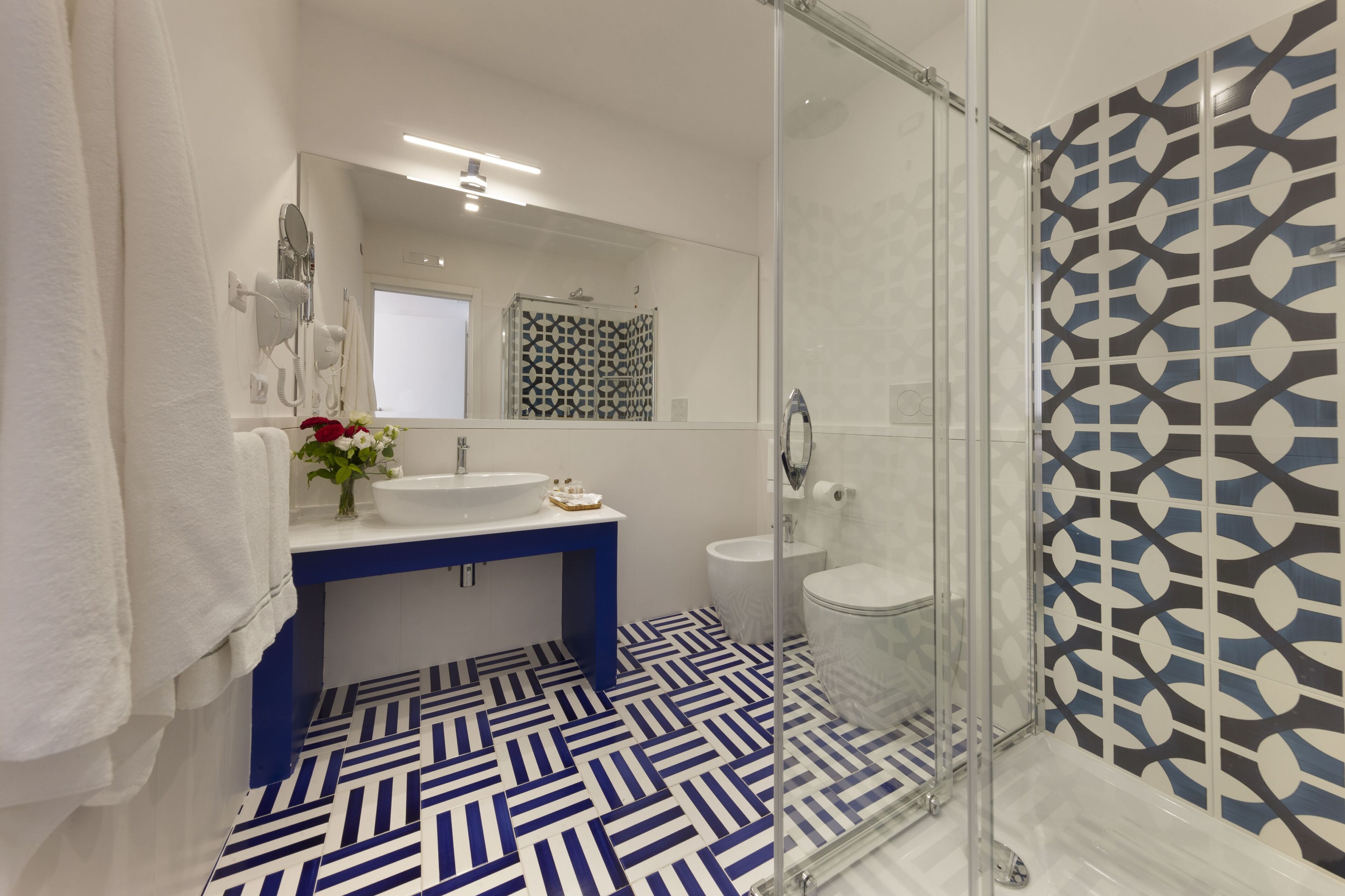 A modern bathroom with a glass shower enclosure, a white sink, and a patterned floor.