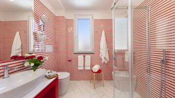 Une salle de bain moderne avec un grand lavabo, une douche en verre et des murs rayés rouges et blancs.