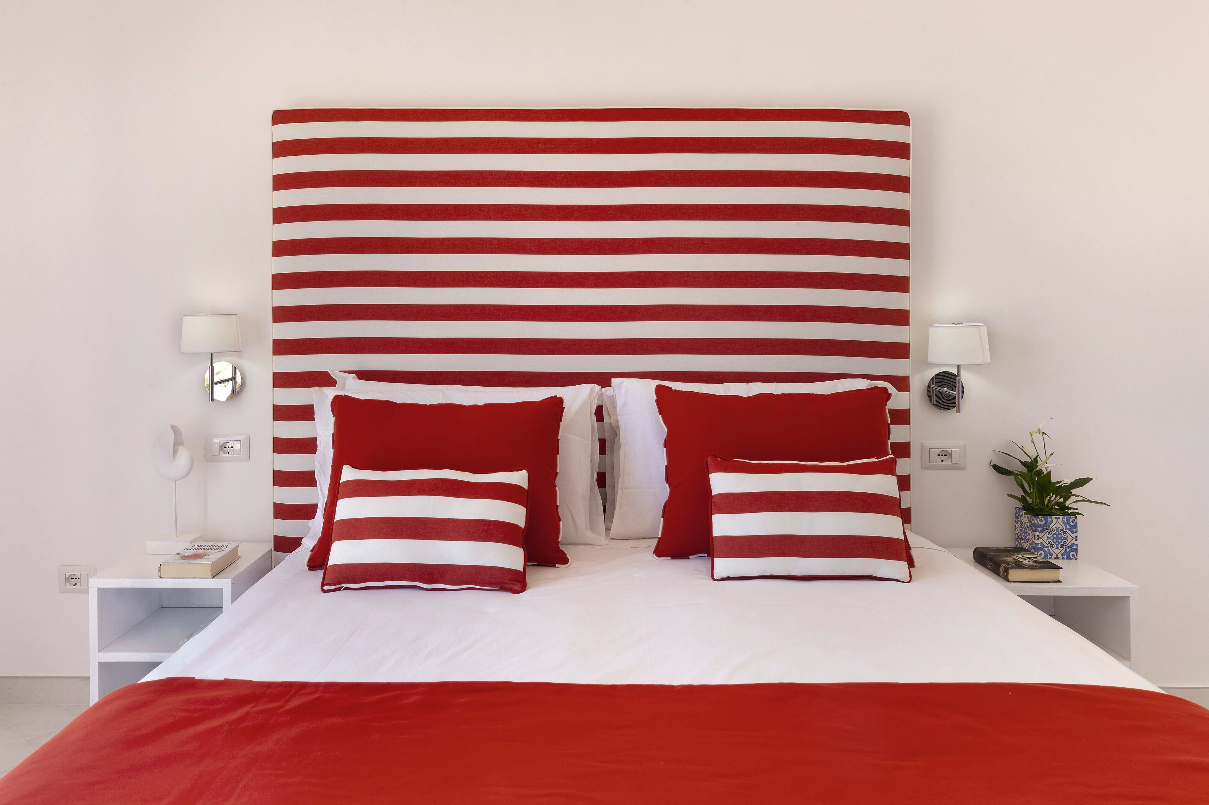 A neatly made bed with red and white striped pillows, a white headboard, and bedside tables with lamps and books.