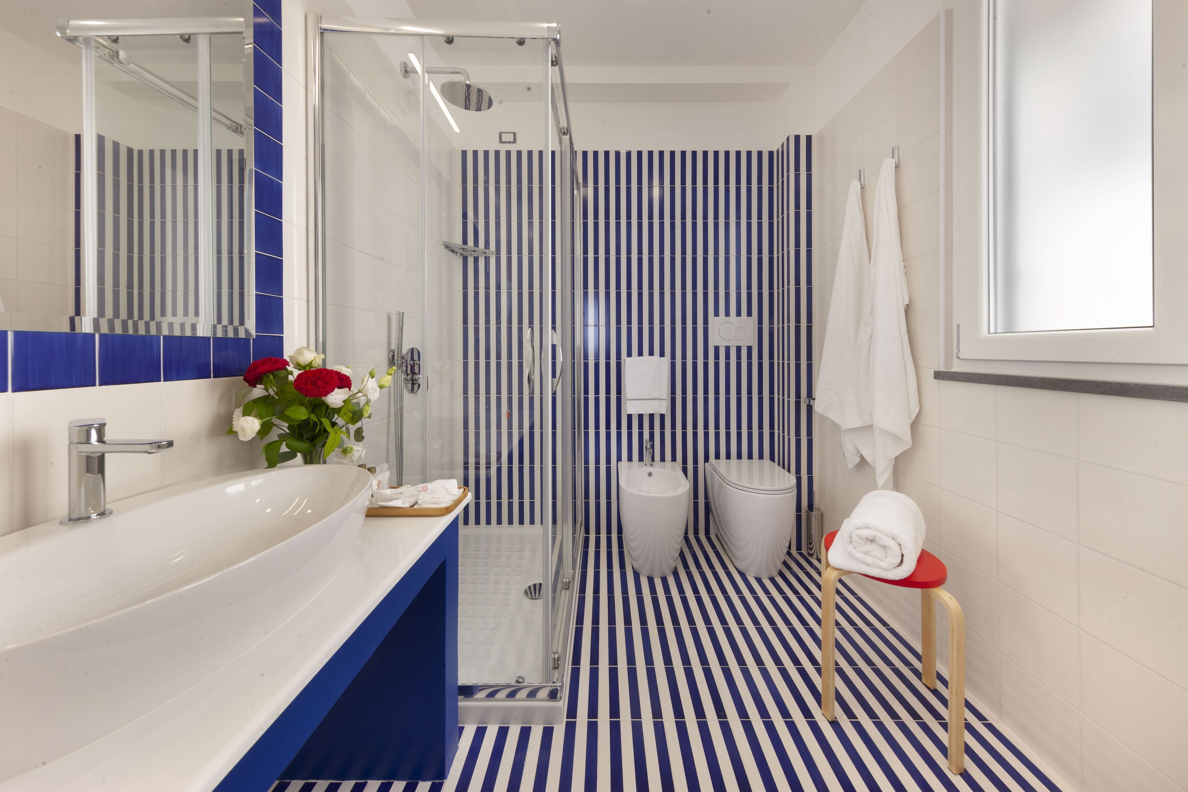 Un baño moderno con un lavamanos grande blanco, cabina de ducha de vidrio y suelo a rayas.