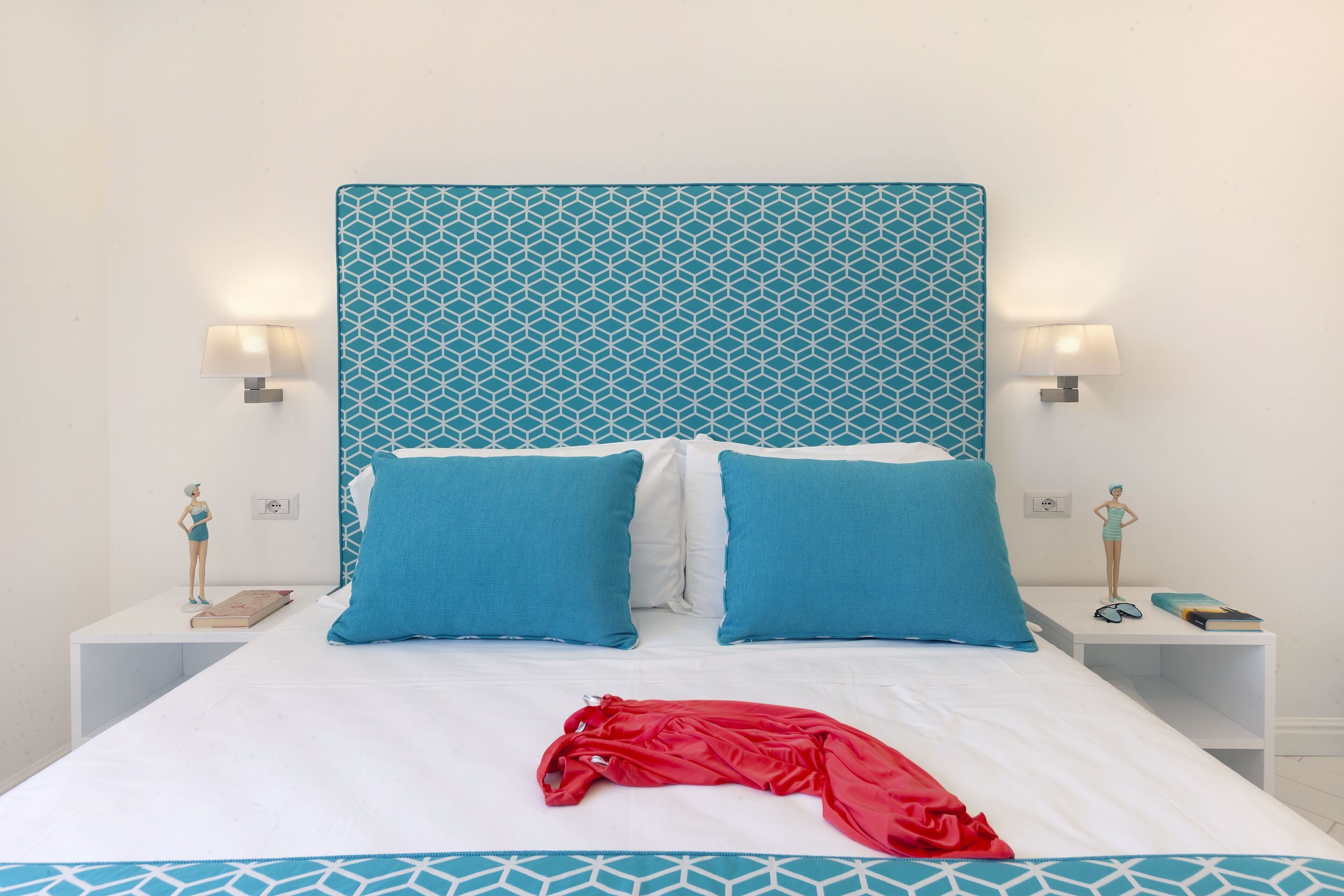 Una cama bien hecha con un cabecero de estampado geométrico, dos almohadas a juego y una prenda roja sobre la cama.