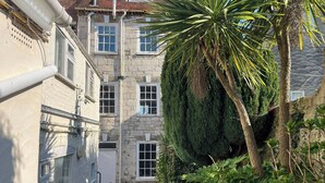A narrow alleyway with stone buildings, a palm tree, and a small seating area with chairs.