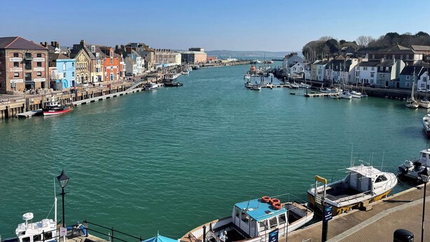 A harbor with boats docked, a pier, and buildings along the waterfront.