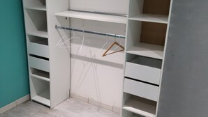 Un armari ampli amb moltes prestatgeries i espai per penjar roba, un llit amb un edredó estampat i una paret color turquesa.