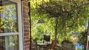 Une terrasse en bois avec une table et des chaises, un luminaire suspendu et un mur en pierre.