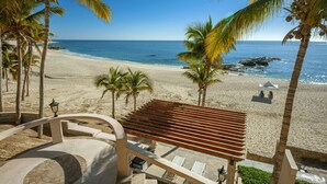 Blick auf einen Strand mit Palmen, einer Holzterrasse und einem weißen Zelt im Sand.