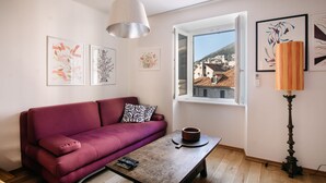 A living room with a red sofa, a wooden coffee table, and a view of buildings through a window.