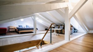 An attic bedroom with a wooden floor, a bed, a red chair, and a sofa.