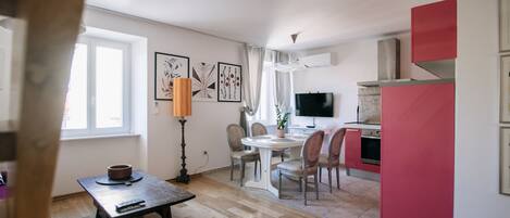 A modern living room with a dining area, a kitchen with red cabinets, and a TV.