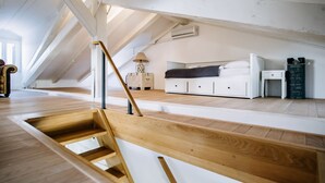 A modern loft bedroom with a wooden staircase, a bed, bedside tables, and a view of the outdoors.