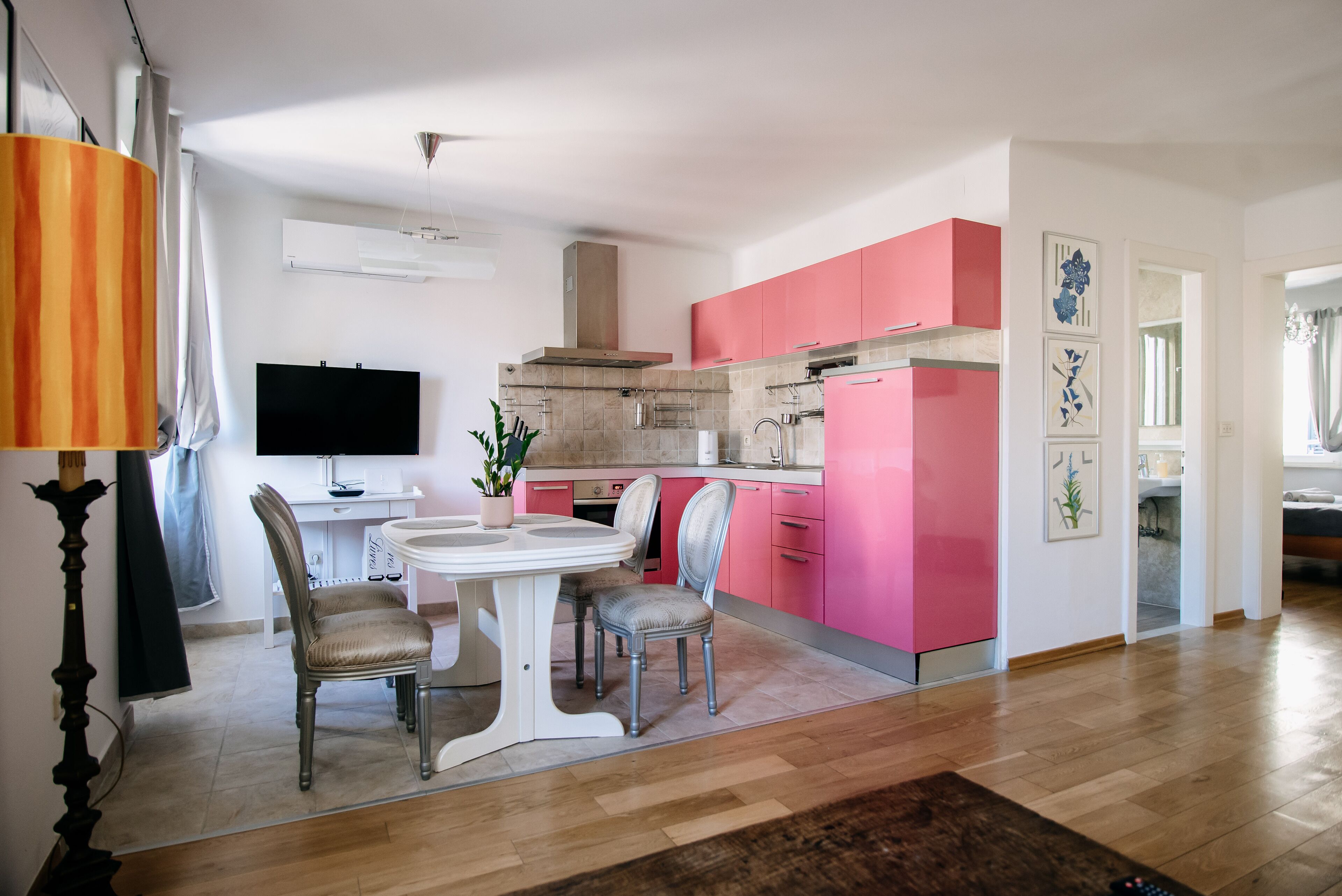 A modern kitchen with pink cabinets, a dining area with a white table and chairs, and a TV in the corner.