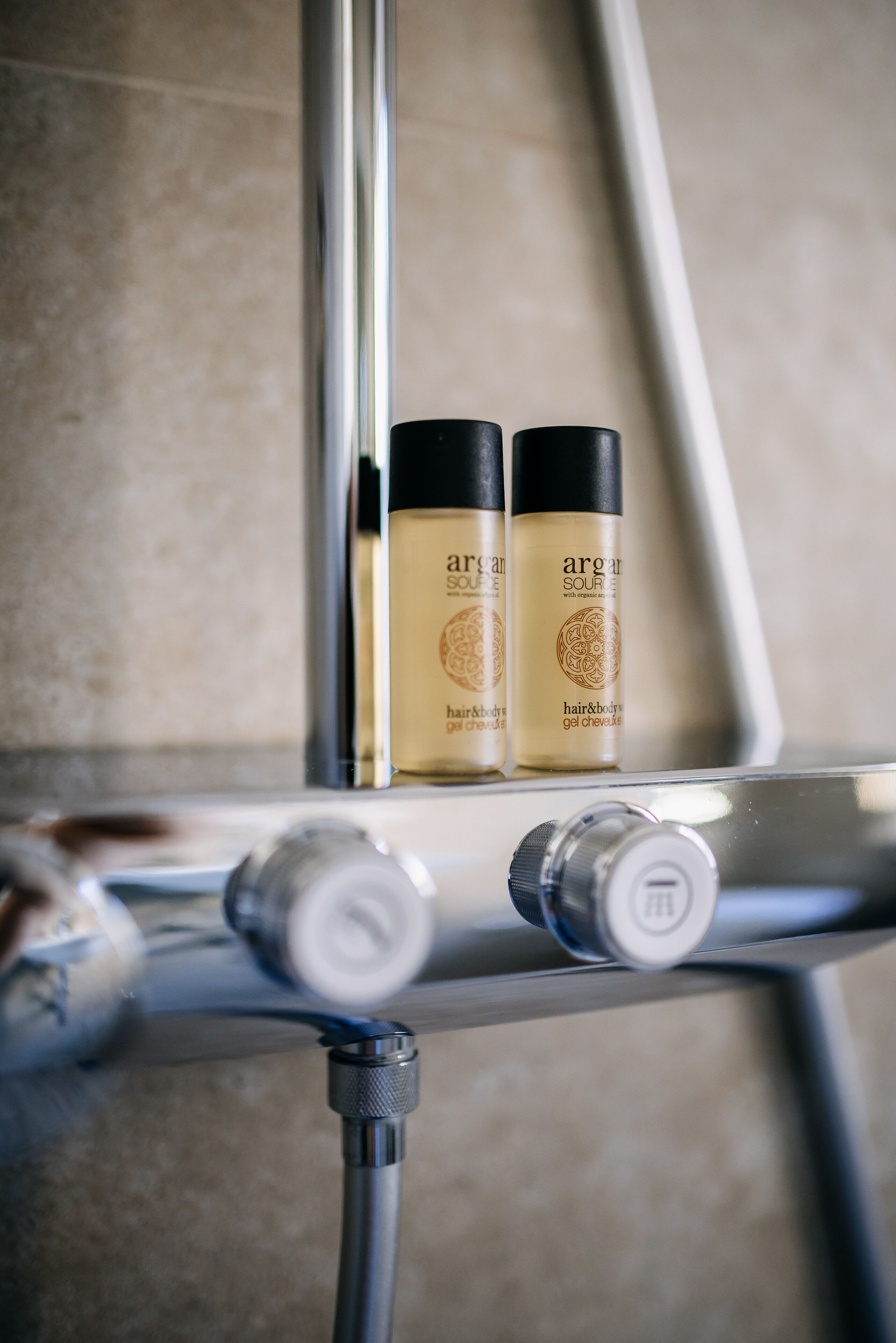 Two bottles of Argan oil on a chrome shelf in a bathroom.