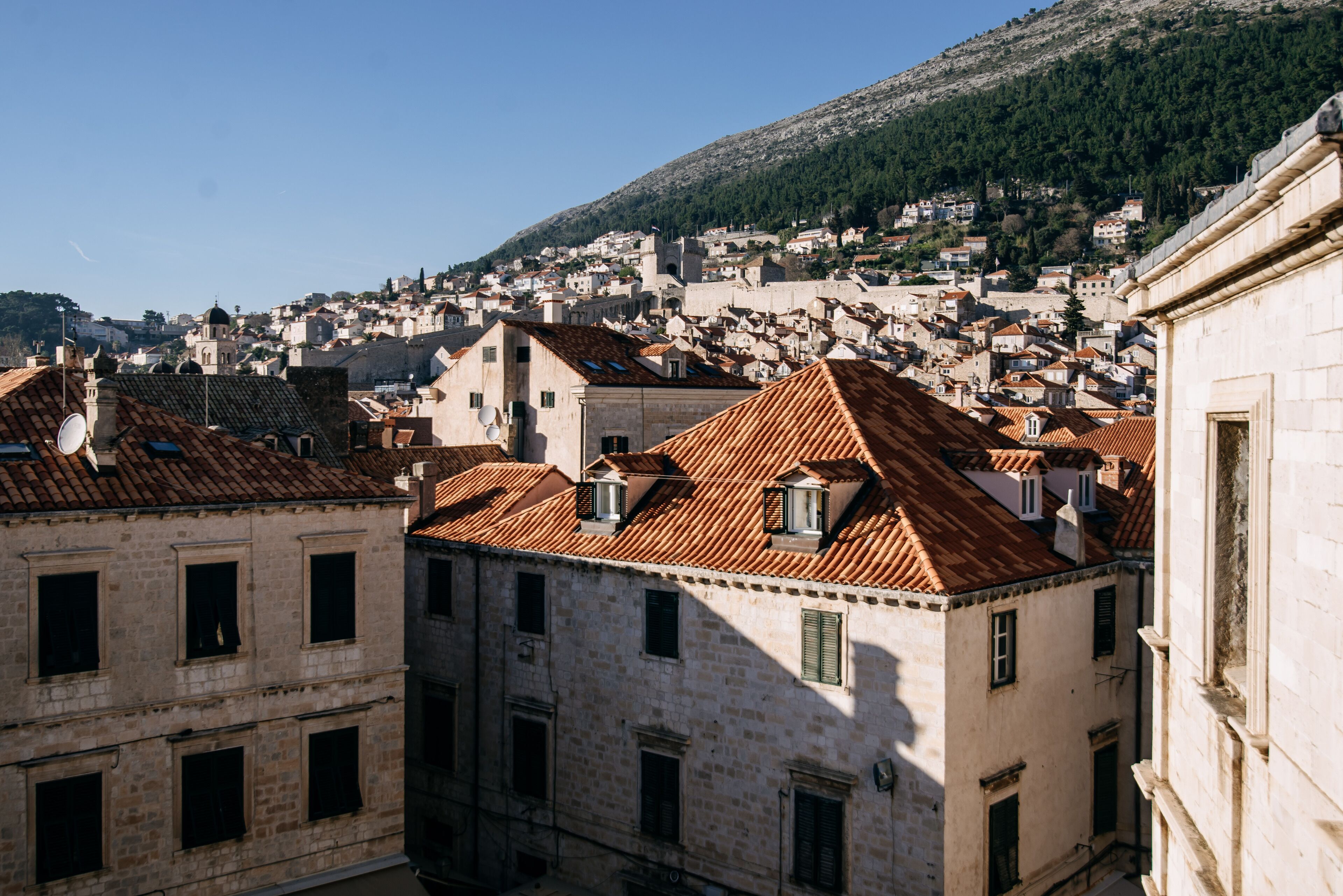 A historic town with terracotta-roofed buildings, narrow streets, and a hillside backdrop.