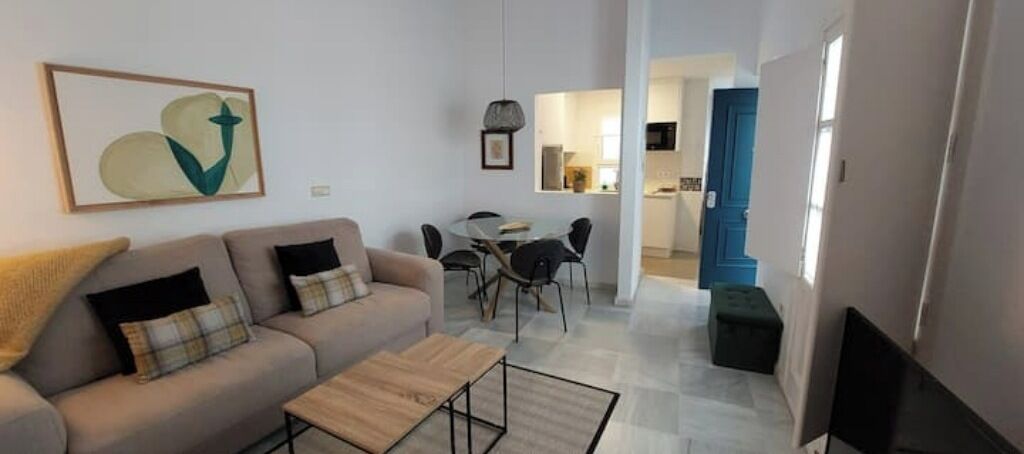 A modern living room with a sofa, coffee table, and dining area with chairs. There is a kitchen visible in the background.