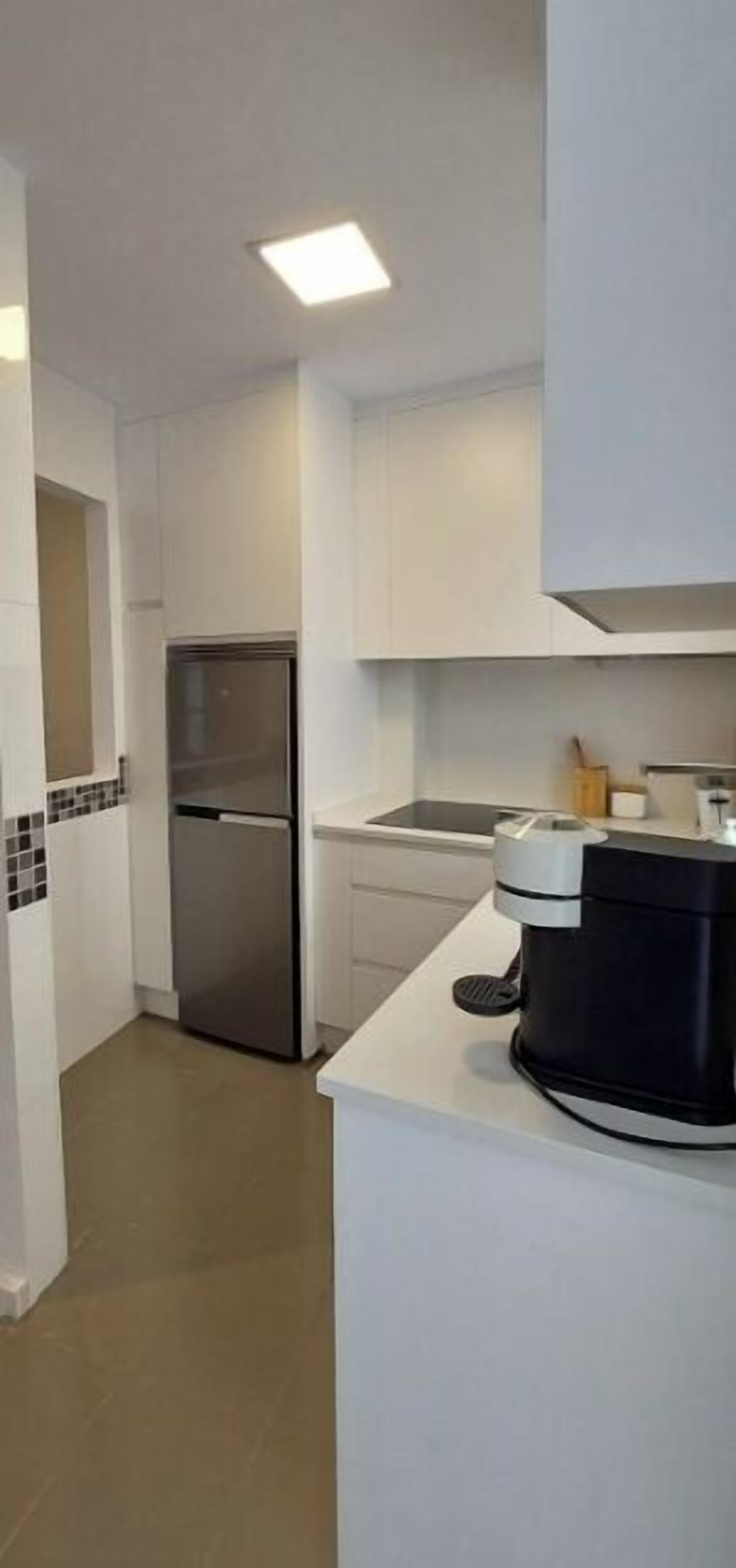 Una cocina moderna con armarios blancos, un refrigerador de acero inoxidable y una cafetera sobre la encimera.