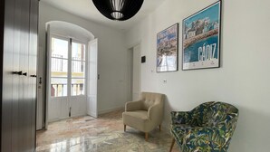 Een ruime hal met een patroon vloer, een beige fauteuil, een kleurrijke fauteuil en twee ingelijste foto's aan de muur.