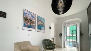 Een gang met een beige fauteuil, een gestreept stoel en twee stadsgezichten in lijsten aan de muur.