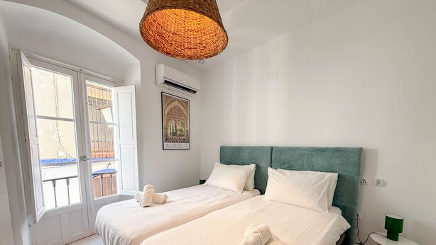 Een hotelkamer met twee bedden, een geweven plafondlamp, een airconditioner, een ingelijst kunstwerk en uitzicht op het balkon.
