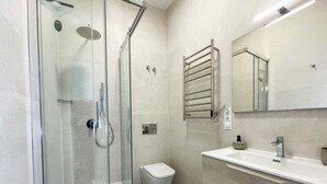 Un baño moderno con ducha acristalada, inodoro, lavabo con espejo y un perchero para toallas.
