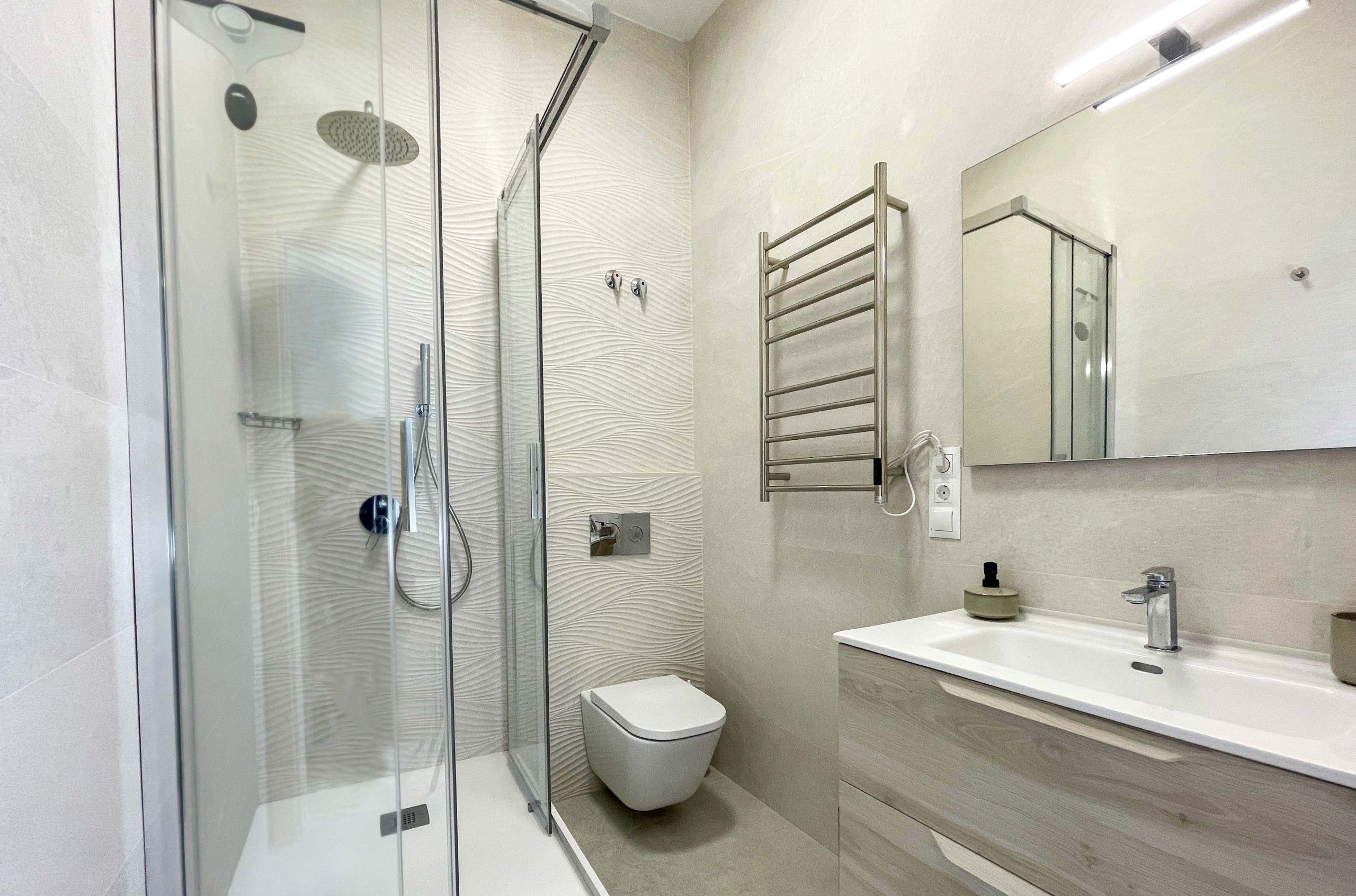 Un bagno moderno con doccia vetrata, un water, un lavandino con specchio e un porta asciugamani.