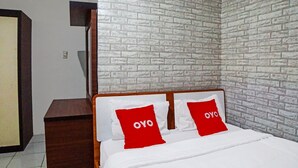 Un dormitorio con pared de ladrillo visto, cabecera de madera y dos almohadas rojas con la palabra 'OYO'.