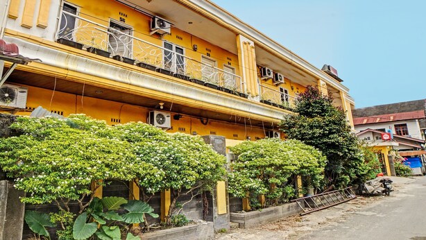 Un edificio amarillo de varios pisos con balcones, unidades de aire acondicionado y un árbol en primer plano.